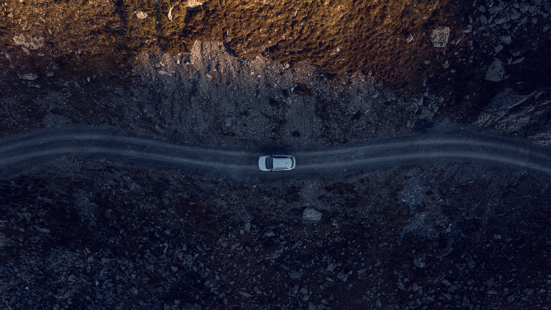 A drone image from above shows a white car on a road in the mountains.