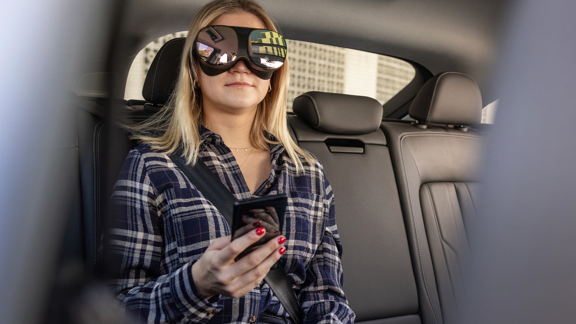 A woman sitting on the back seat of a vehicle using holoride technology via a VR headset.