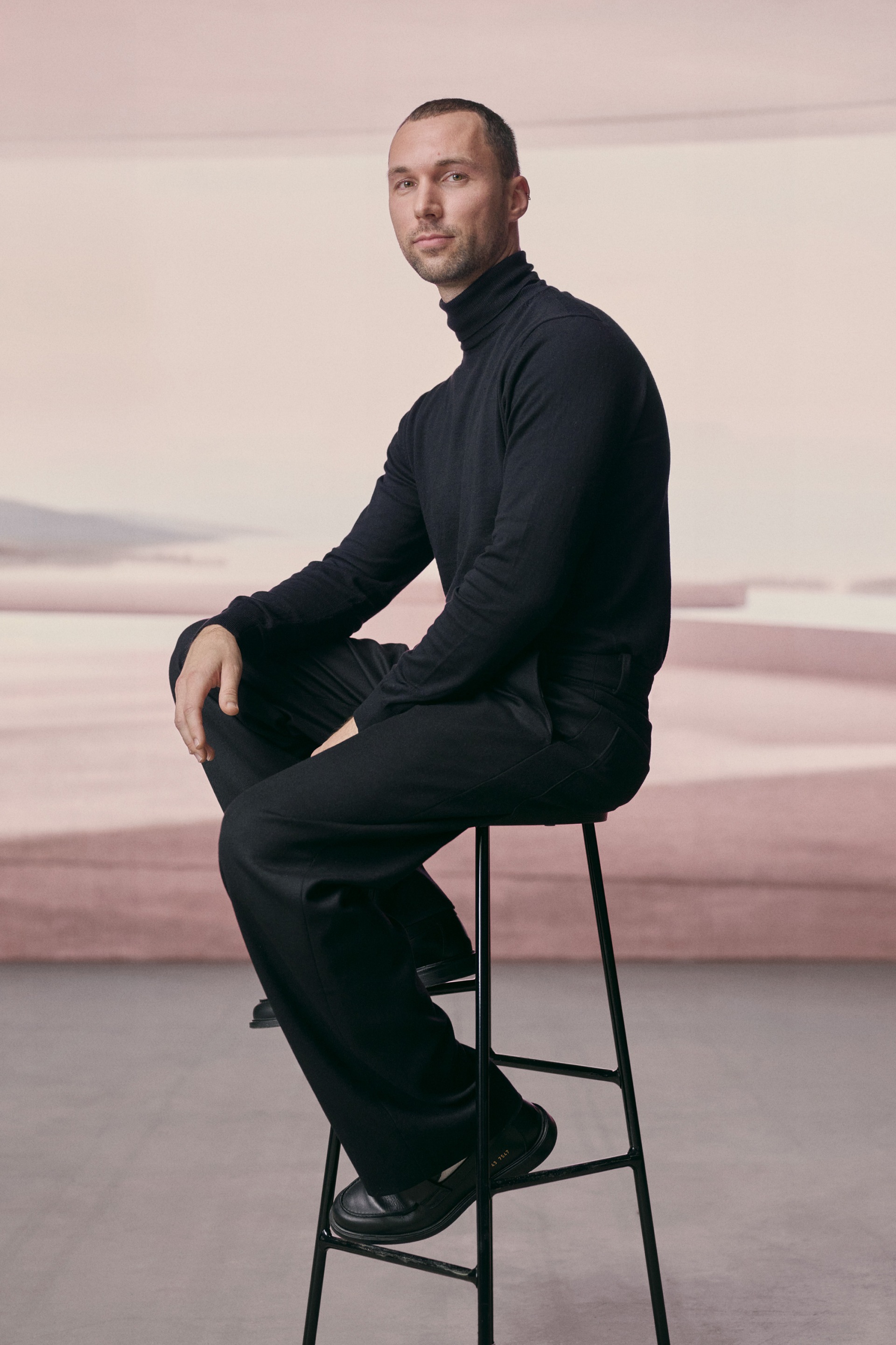 Portrait of Andrés Reisinger sitting on a bar stool.